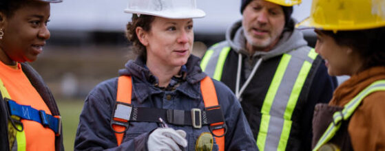 A small group of constructions workers huddle together as they take instructions from the site supervisor. They are each wearing proper protective gear and are listening attentively. how to choose the right architects and engineers