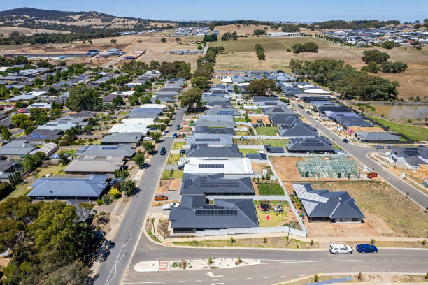 Aerial close view new rural housing development being constructed alongside established housing suburb in Mt Barker, near Adelaide, South Australia. Left of frame established streets with street trees and landscaped gardens. Right of frame, new houses and construction sites with few trees and landscaping. Solar panels installed on some properties. In the foreground backyards, a clothesline with drying washing, trampoline, and a lush green crop. In the distance, Mt Barker looms over the rolling rural hills with other pockets of separate development visible. What is Community Plan Mean in Los Angeles: A Guide for Property Owners and Developers