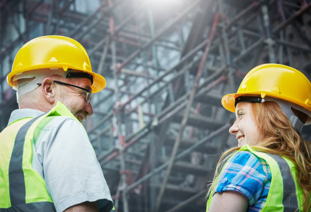 A young female construction worker and her older male mentor smile at each other on a construction site. Construction Consulting Firms in Los Angeles