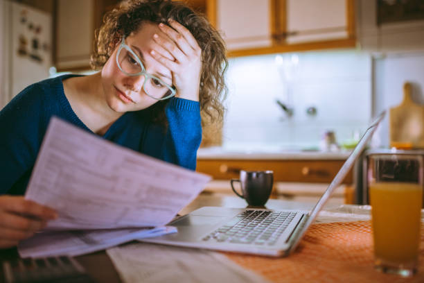 Young female reading documents, using laptop in the kitchen at home