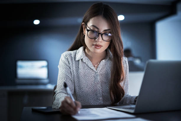 Shot of a young businesswoman going through paperwork while working in an office at night