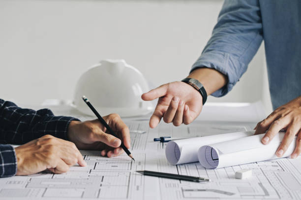 Two business man construction site engineers. working drawing on blueprint and discussing the floor plans over blueprint architectural plans at table in a modern office. construction concept, benefits of hiring construction consultant