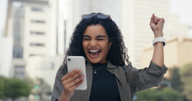 Woman, smartphone and celebration for win in city, online competition and discount or promotion. Female person, fist pump and excited for opportunity on mobile app, lottery prize and virtual giveaway