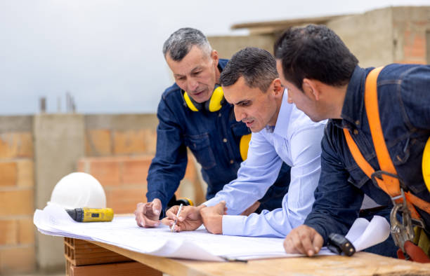 Site Plan Review, Latin American architect talking to construction workers while looking at a blueprint at a construction site