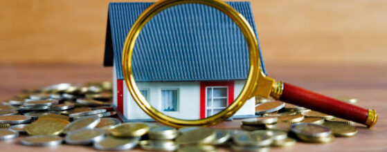 A house on coins, a magnifying glass highlighting details – a symbol of real estate appraisal, hidden costs, and potential defects that should be checked before buying