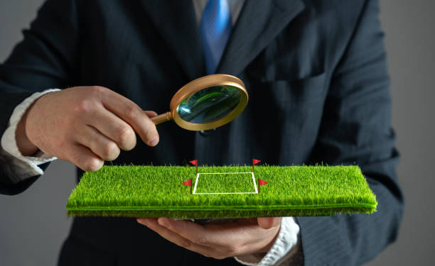 A businessman examines a plot of land with a magnifying glass. Purchase and sale of land. Plot valuation. Checking for arrests and possible risks to the successful conclusion of the contract.