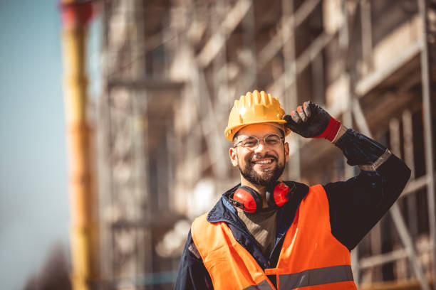 Construction site manager standing wearing safety vest and helmet, thinking at construction site. Young architect watching construction site with confidence.