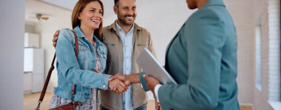 Happy woman shaking hands with real estate agent while buying new apartment with her husband, illustrating the role of real estate consultant
