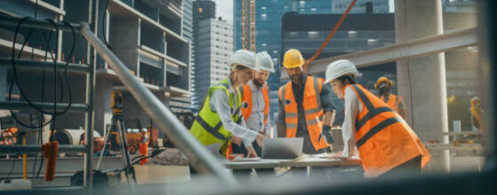 Female Civil Engineer Using a Laptop Computer and Talking with General Workers at a Residential Building Title 24 California