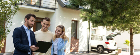 Real estate agent presenting clipboard with documents to couple in front of residential property in suburban outdoor setting