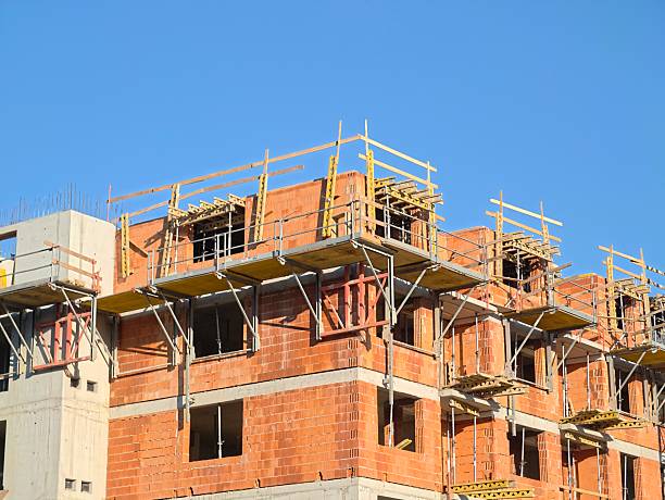 building site under open sky, orange brick structure with scaffolding shadows against bright blue